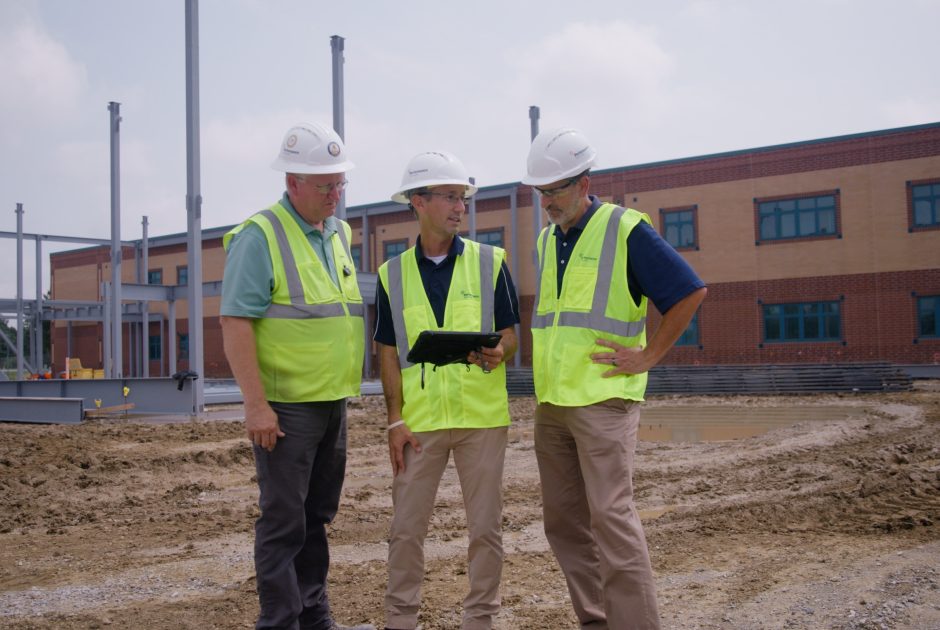 Three architectural team staff in safety vests and hardhats looking at design plans on a jobsite