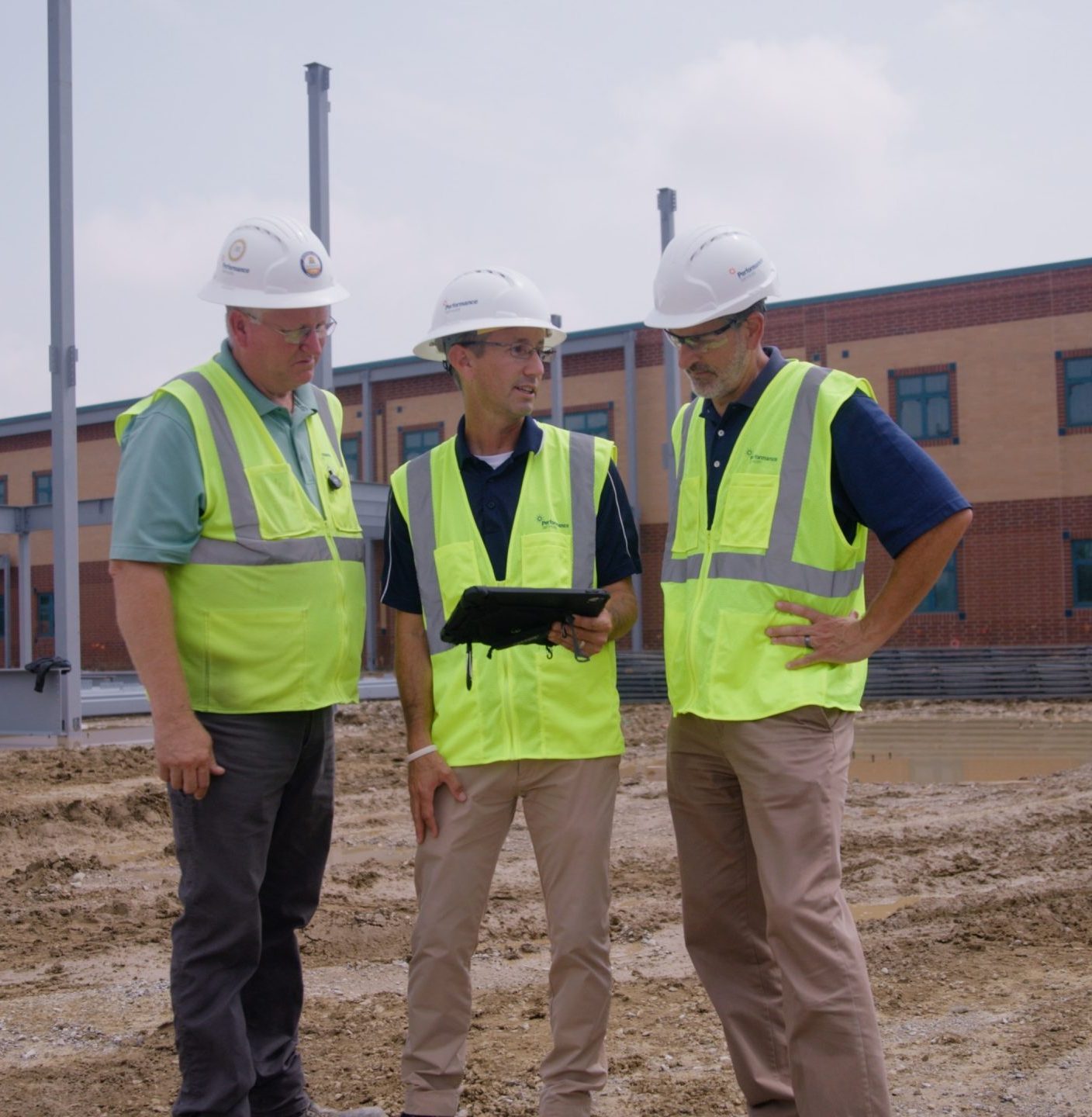 Three architectural team staff in safety vests and hardhats looking at design plans on a jobsite