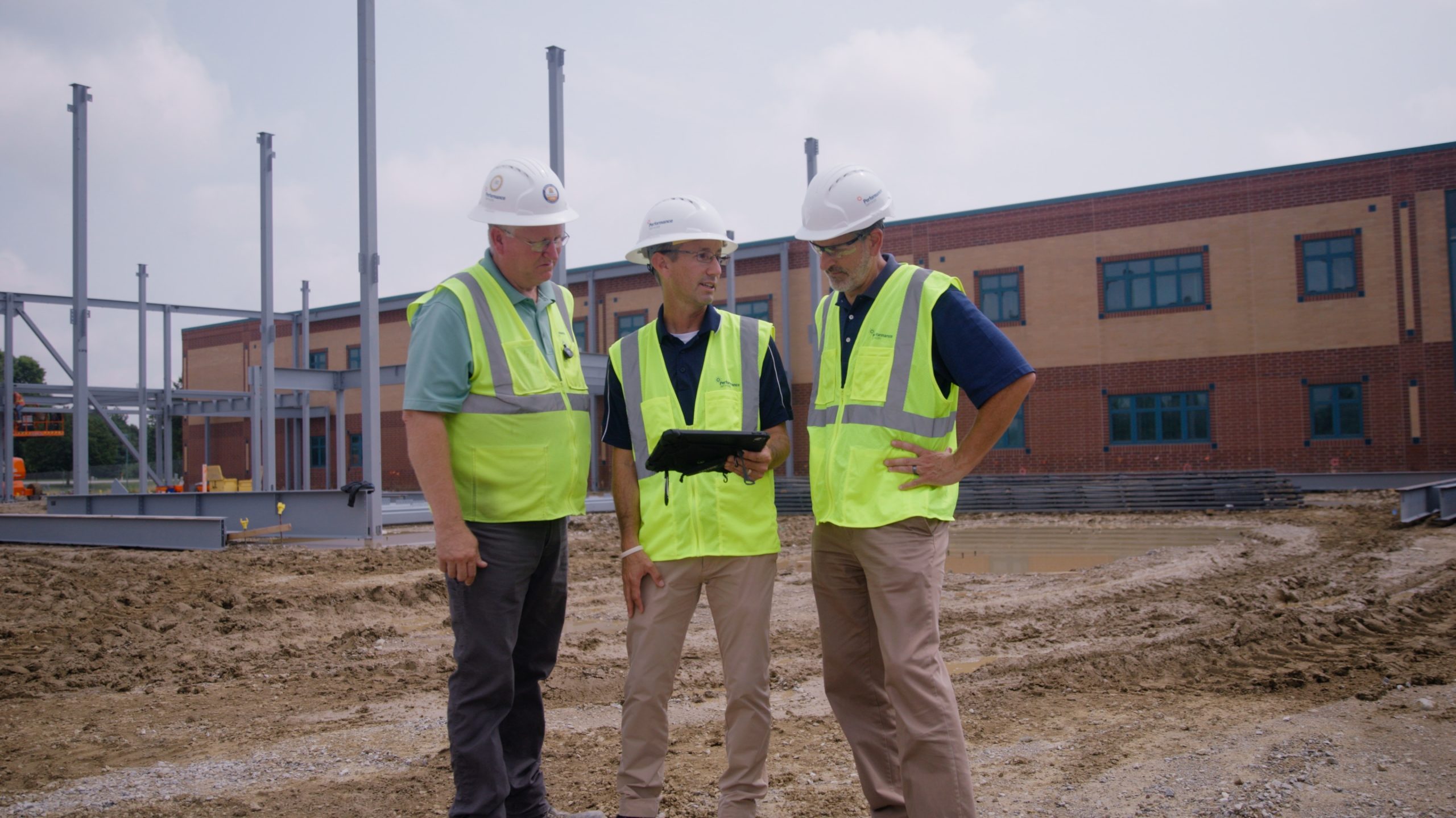 Three architectural team staff in safety vests and hardhats looking at design plans on a jobsite