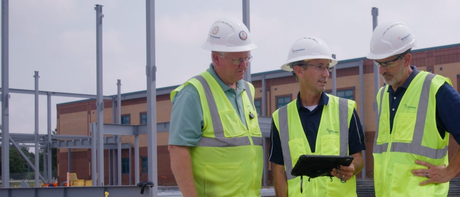 Three Performance Services architects collaborating on an active construction site in hard hats and safety vests